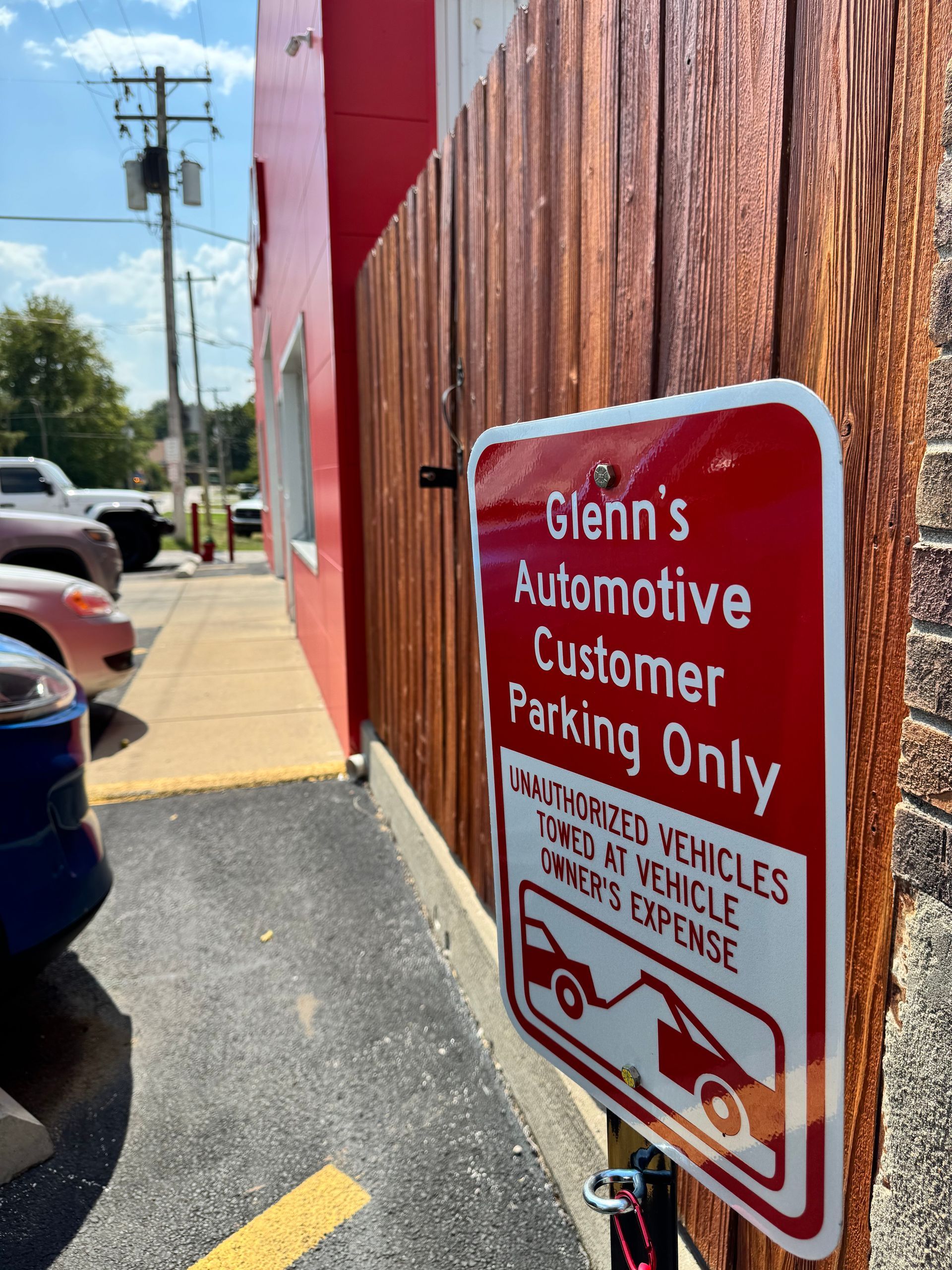 Red customer parking only sign on a brick wall beside a sidewalk and parked cars