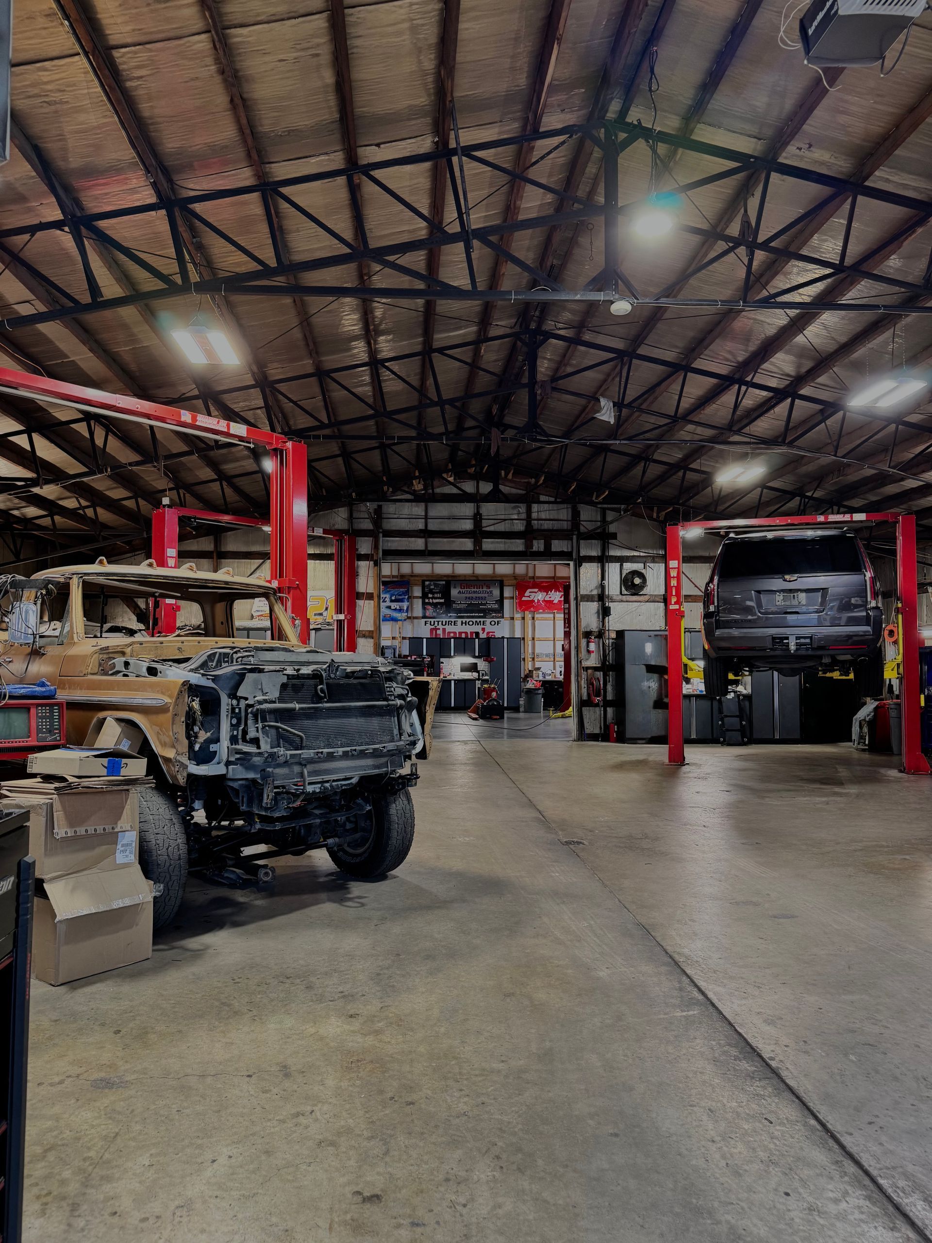 Auto repair garage with raised vehicles, red lifts, and an exposed metal roof