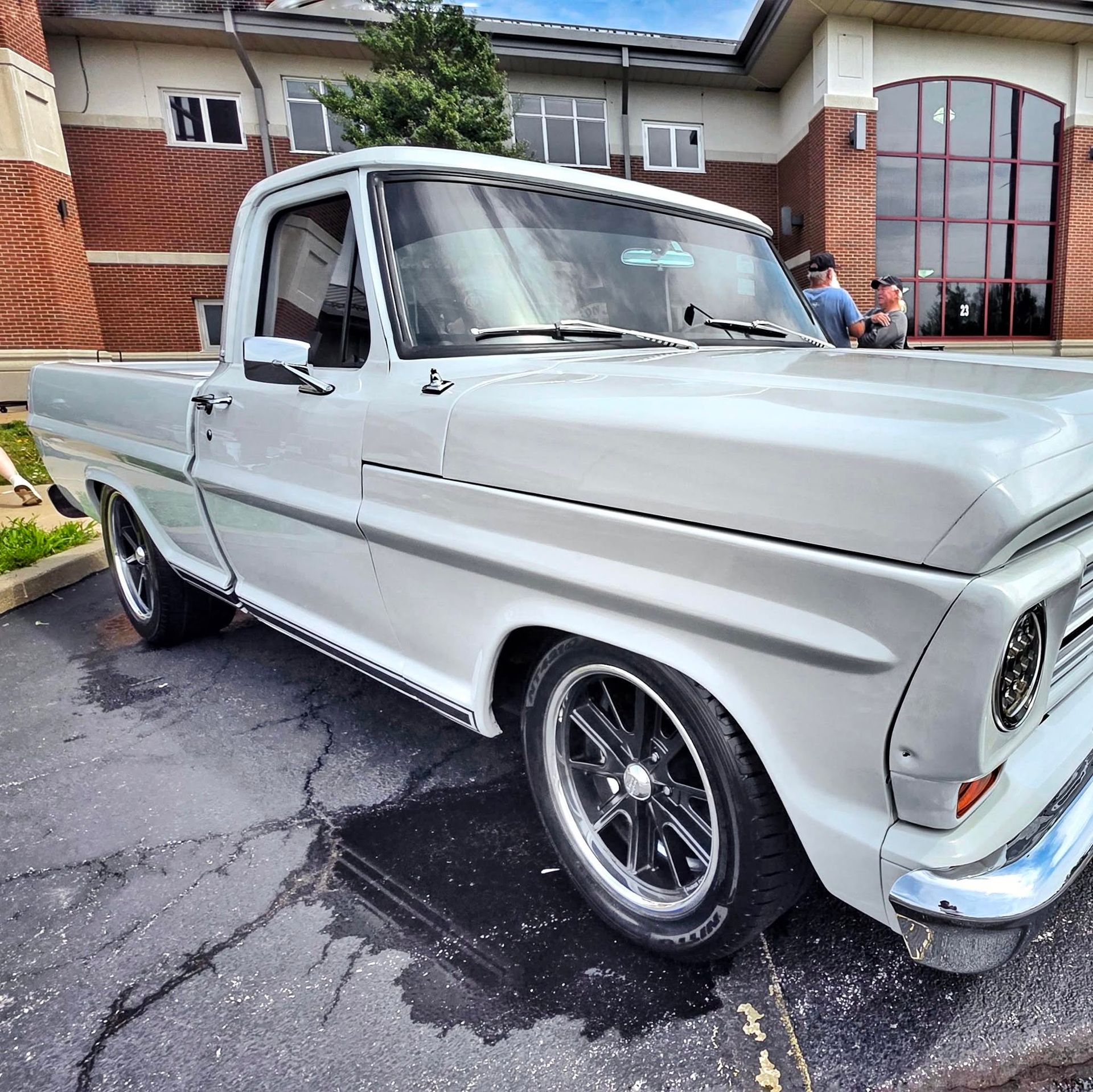 Classic white pickup truck parked outside a brick building on a wet driveway
