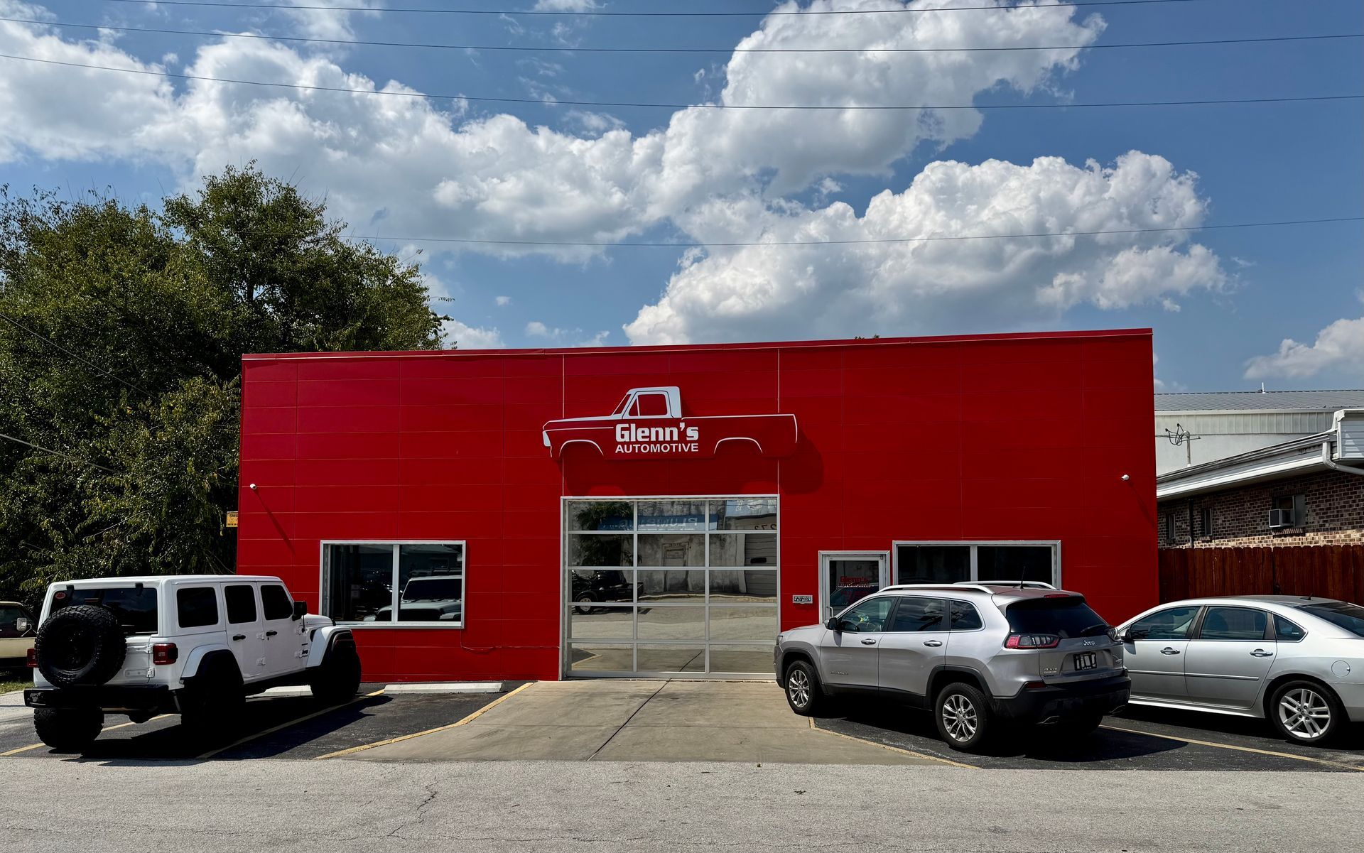 Red auto service building with parked vehicles under a cloudy blue sky
