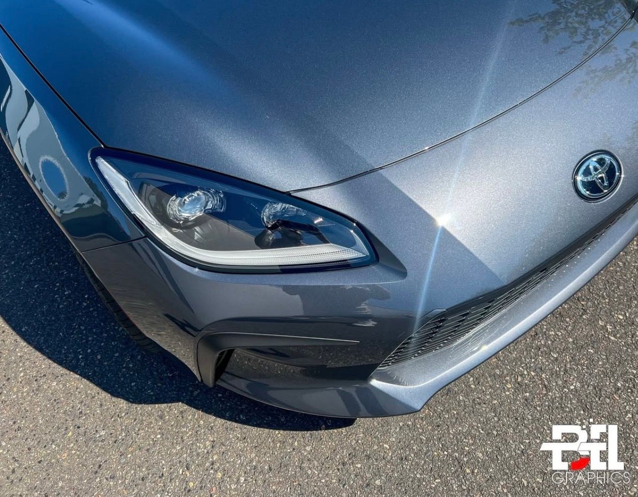 Gray Toyota GR86 sports car front, close up; headlights and Toyota emblem visible.
