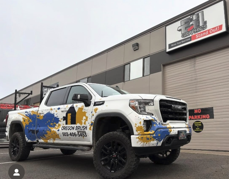 White GMC pickup truck with company logo parked outside a business. Blue and yellow paint splatter design.