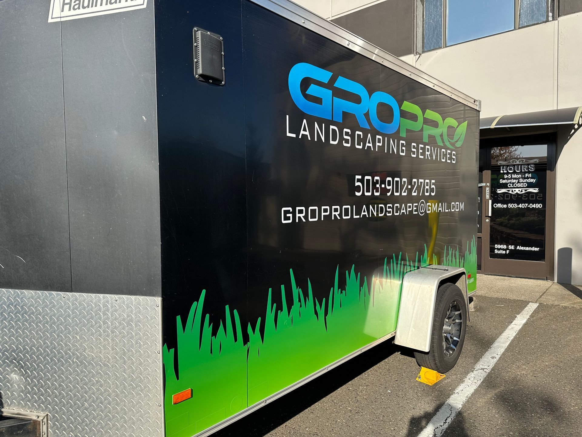 Black GroPro landscaping trailer with green grass design parked in front of a building.