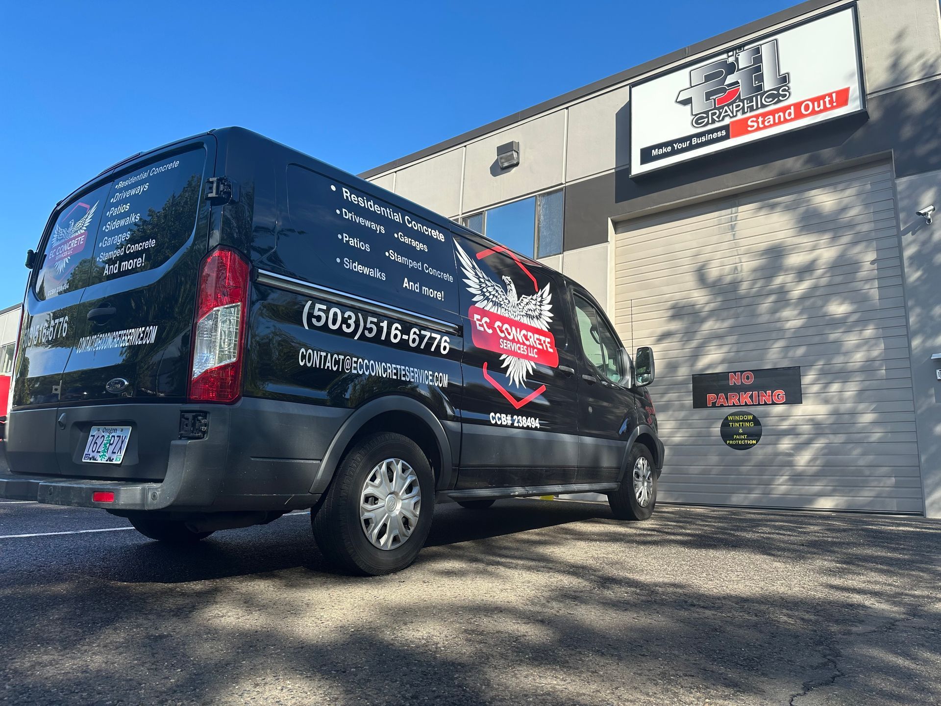 Black van parked outside a building with a sign. The van has business information and a phone number displayed on it.