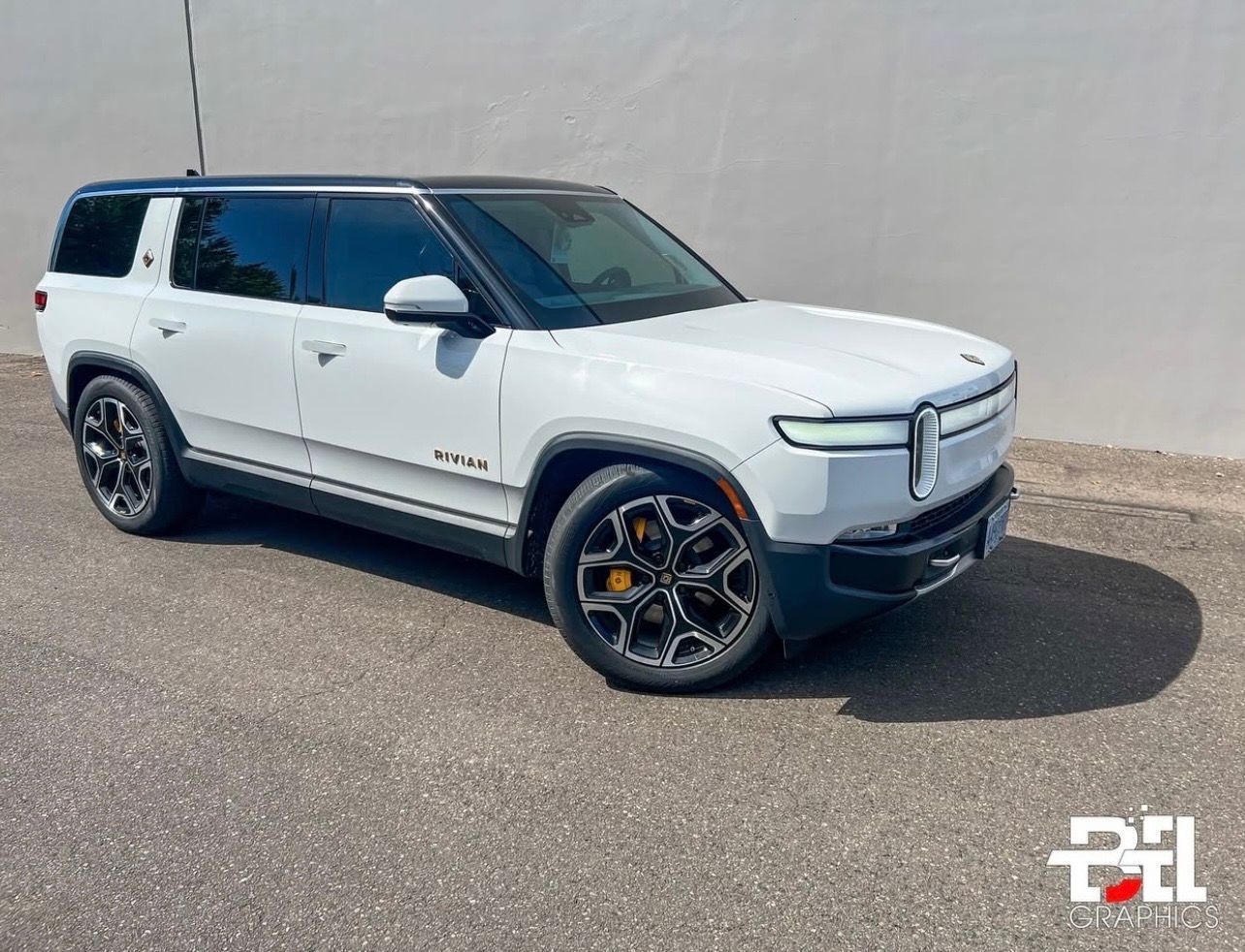 White Rivian SUV parked on asphalt. Black roof and accents, dark wheels with gold calipers.