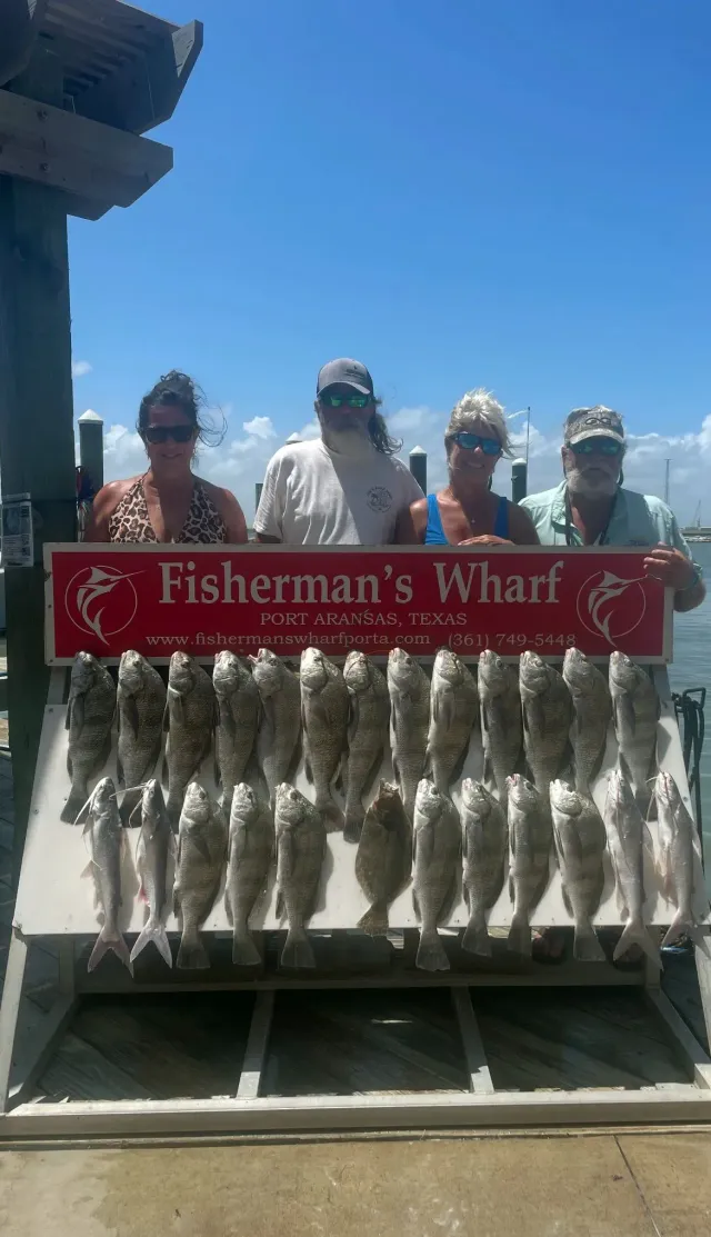 Four people pose with a large catch of fish at Fisherman's Wharf under a blue sky.
