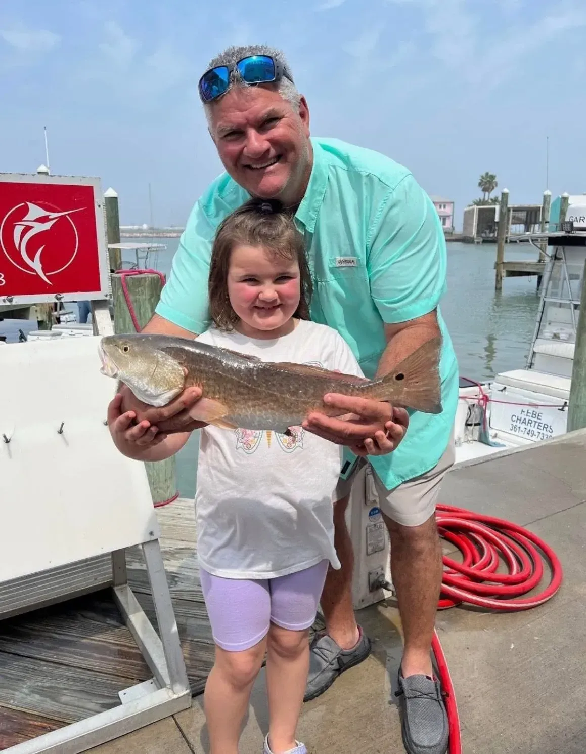 Man and child holding a red fish on a dock. Smiling, sunny day.