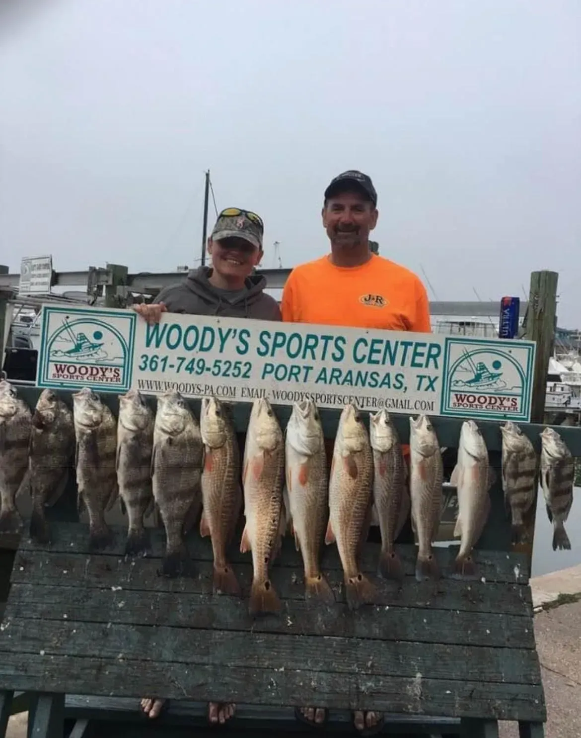 Two people pose with fish at Woody's Sports Center in Port Aransas, TX. Variety of fish on a board.