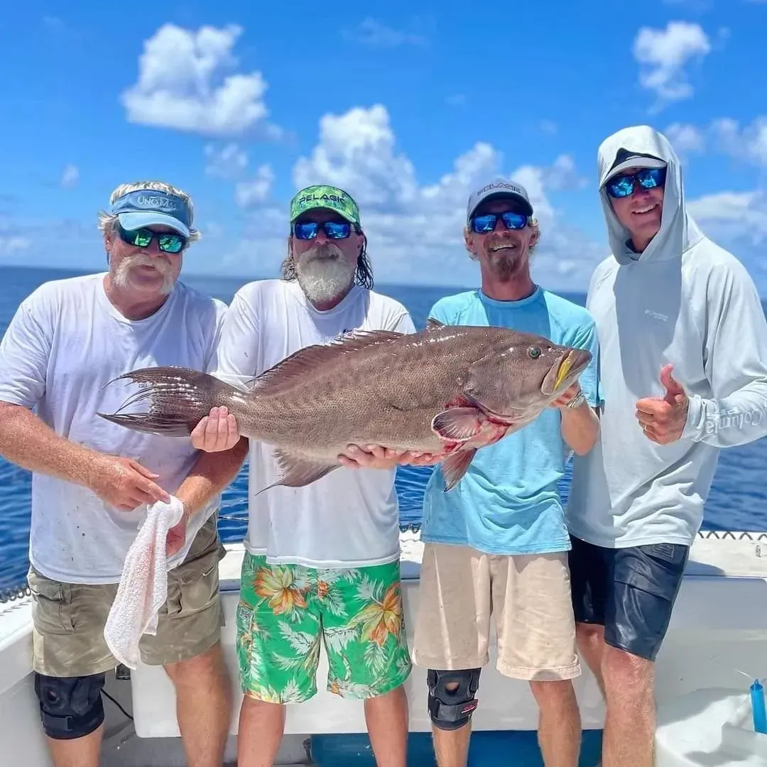 Four people on a boat display a large fish, blue water and sky background.