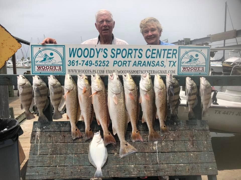 Two people posing behind a rack of caught fish with a Woody's Sports Center sign.
