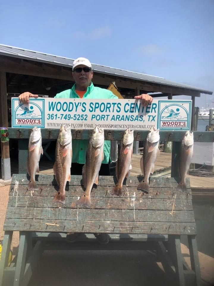 Man holding a sign for Woody's Sports Center with six fish displayed on a wooden rack, Port Aransas, TX.