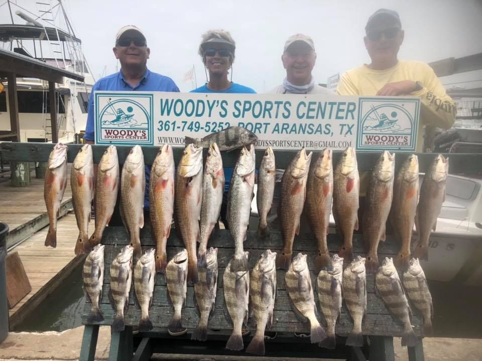 Four people holding a wooden rack with caught fish at Woody's Sports Center in Port Aransas, TX.