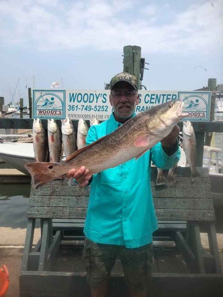 Man holding a large redfish at Woody's Fishing Center, with other caught fish displayed.