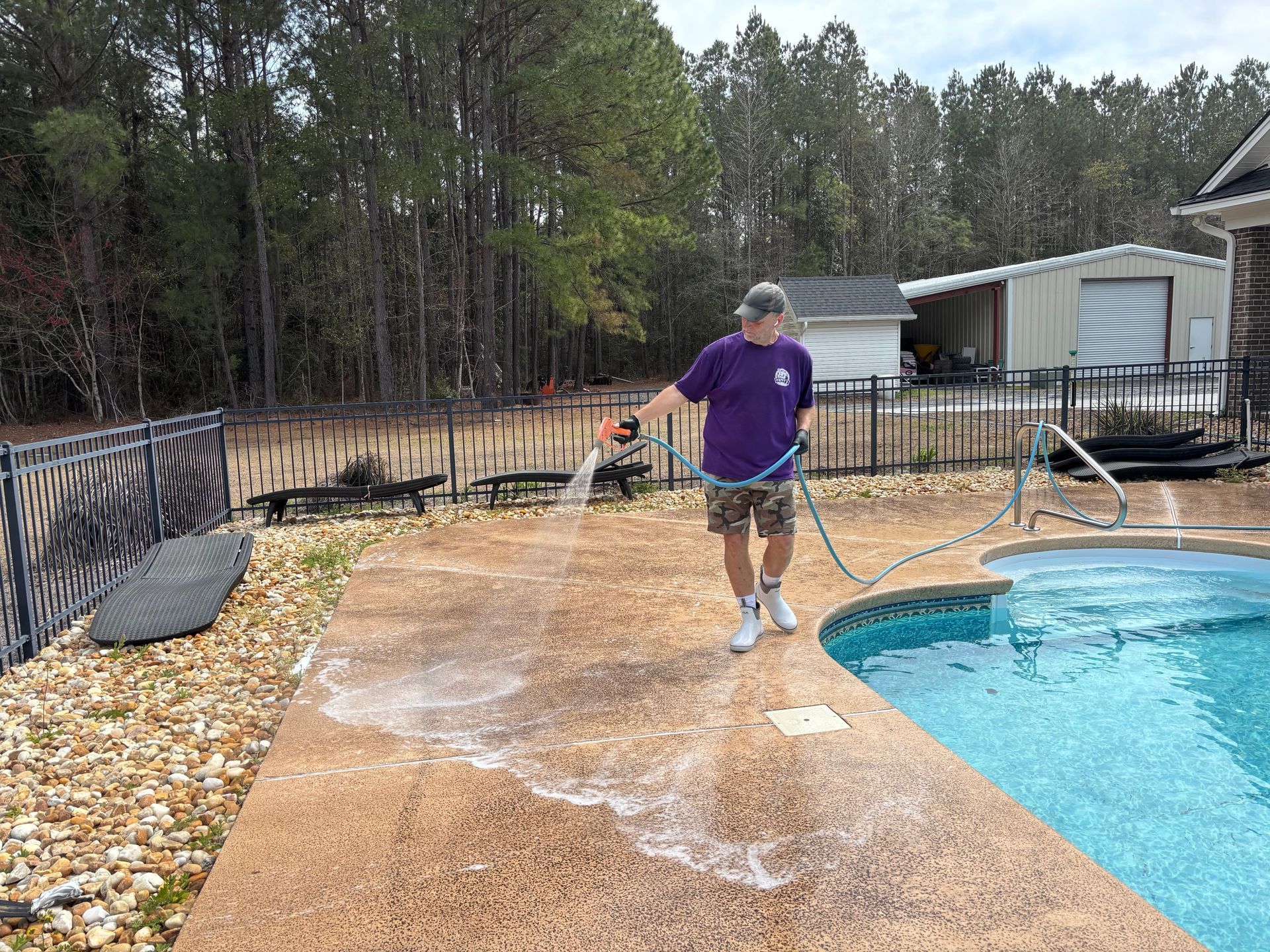 A man in a purple shirt is cleaning a pool with a hose