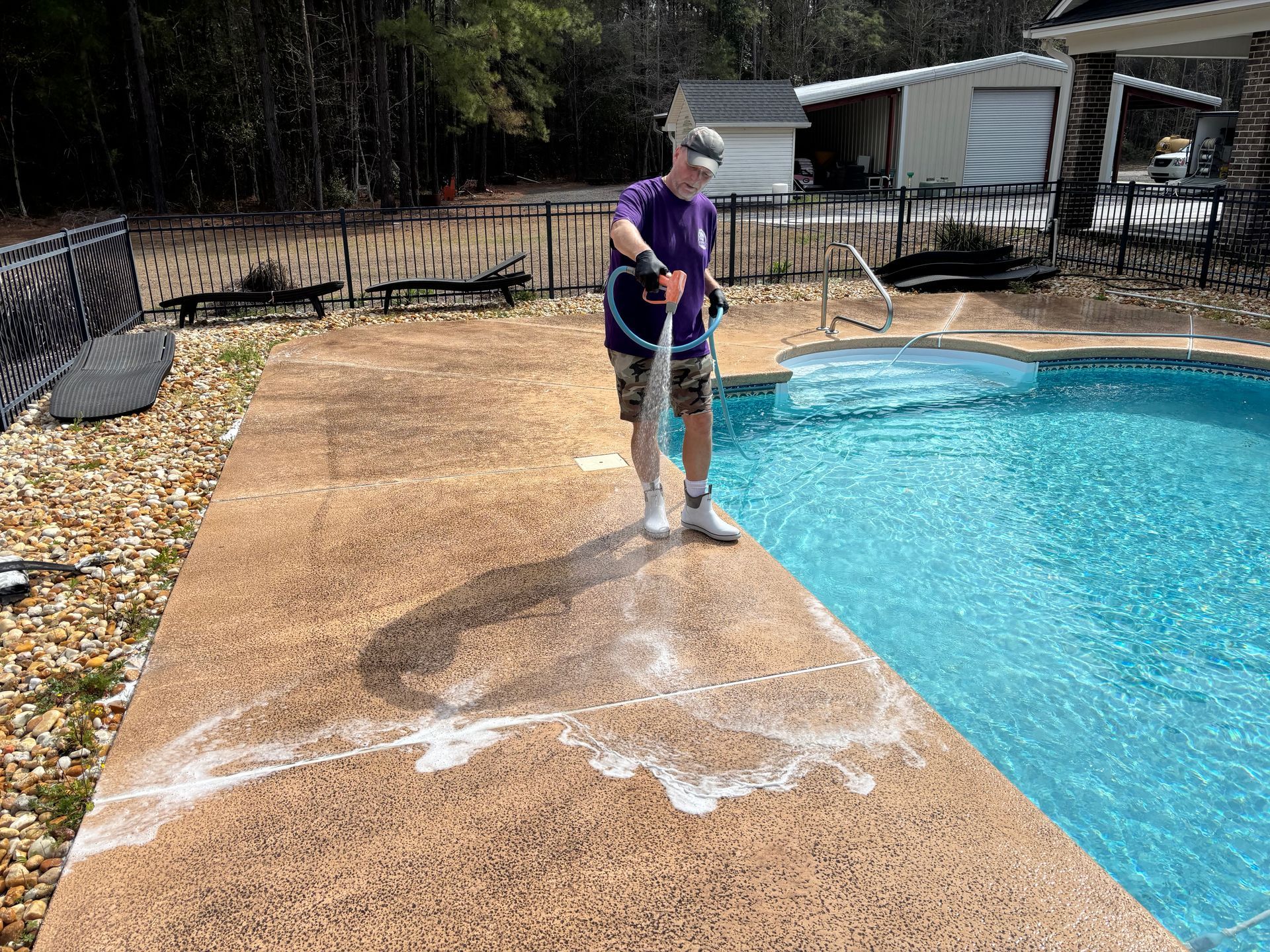 A man is cleaning the sidewalk next to a swimming pool