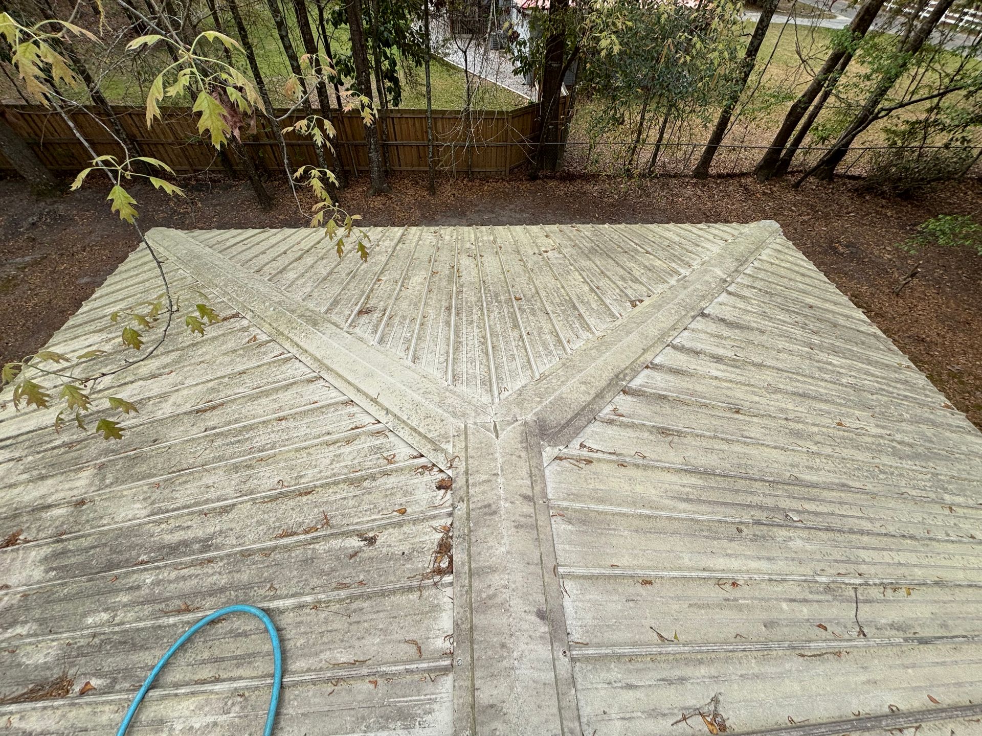 A wooden deck with a blue hose on it and trees in the background