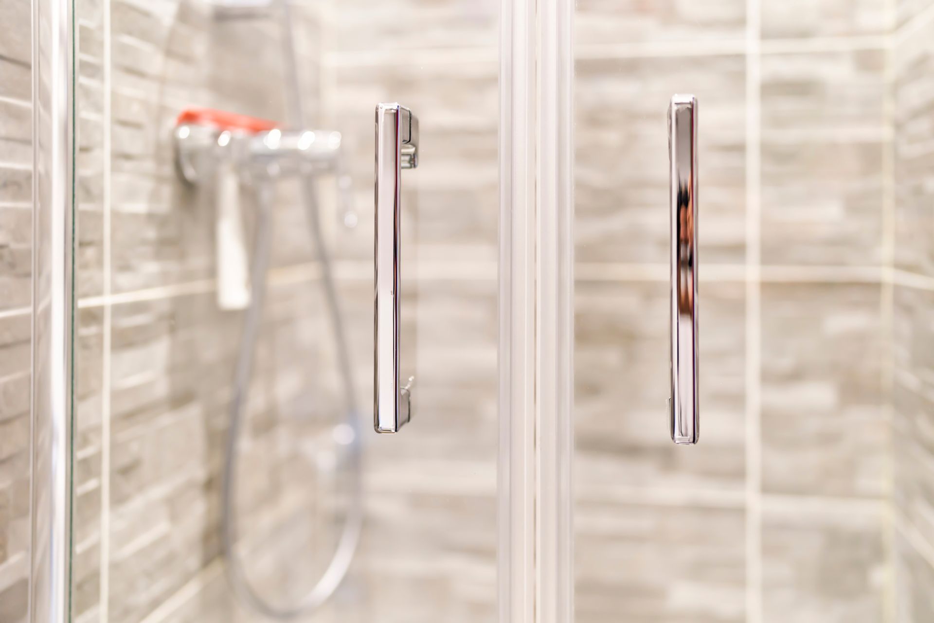 Chrome shower door with silver handles, in front of a tile wall.