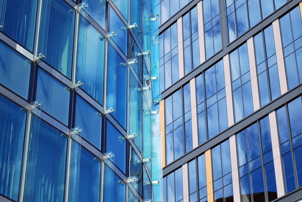 Blue glass facade of a modern building, reflecting sky and adjacent structure.