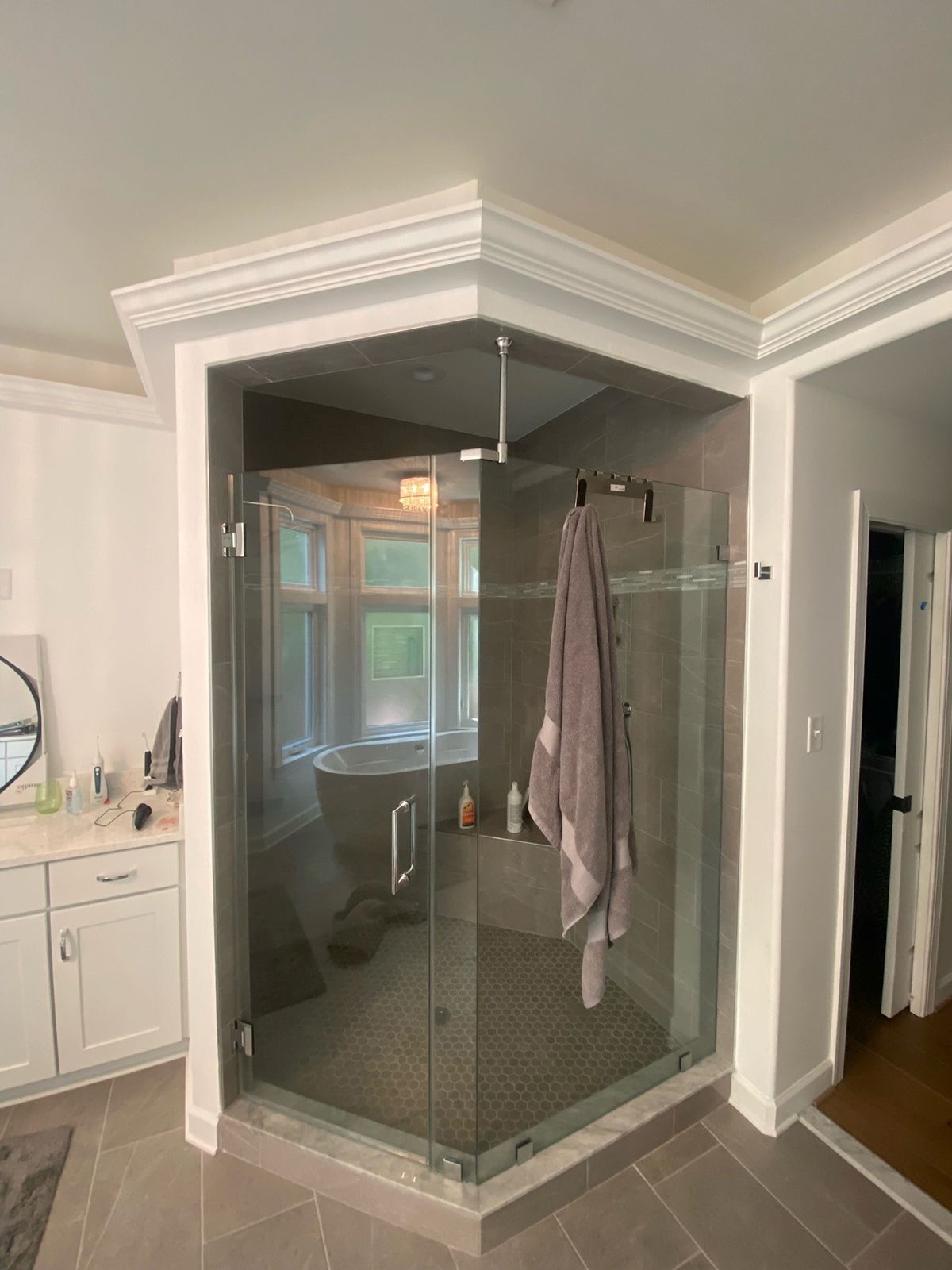 A corner glass-enclosed shower with a gray-tiled interior, a towel hanging on the door, and a white vanity to the left.
