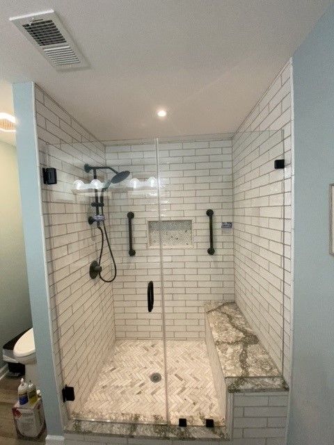 Accessible shower with white subway tile, glass doors, and a built-in bench. Black hardware and grab bars are visible.