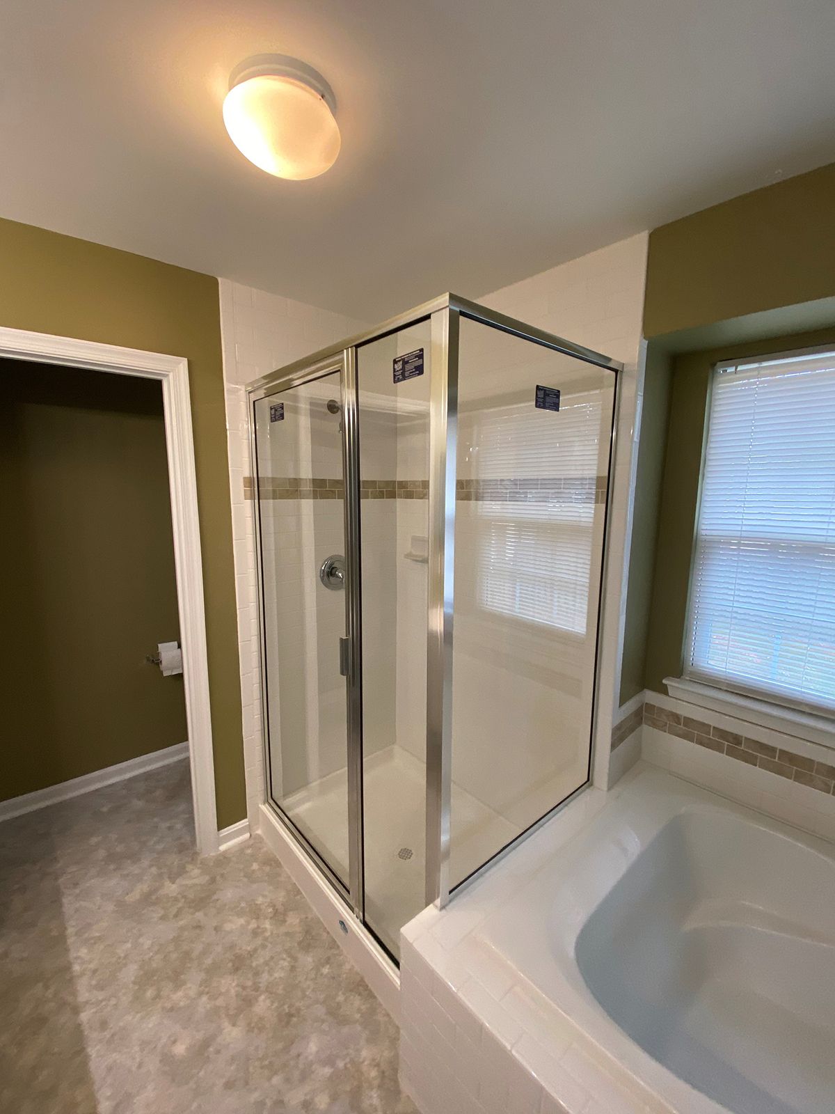 A bathroom featuring a glass-enclosed corner shower, a white bathtub, and olive green walls under a ceiling light.
