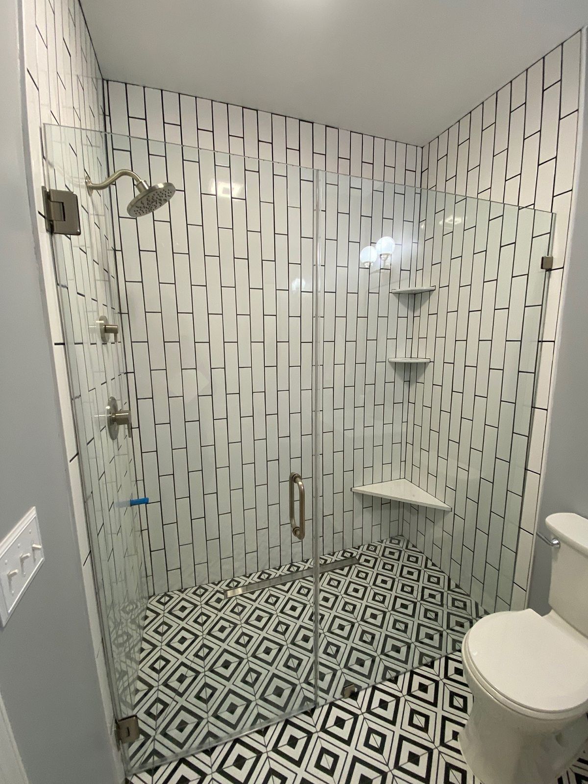 A walk-in shower with black and white geometric floor tiles and patterned wall tiles, featuring a glass door and toilet.