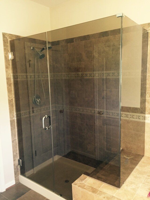 Glass shower enclosure with brown tile walls and tan flooring. Chrome shower fixtures.