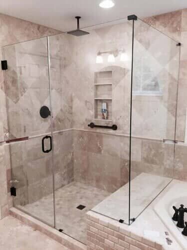 Glass-enclosed shower in a beige-tiled bathroom. Black fixtures and a built-in bench.