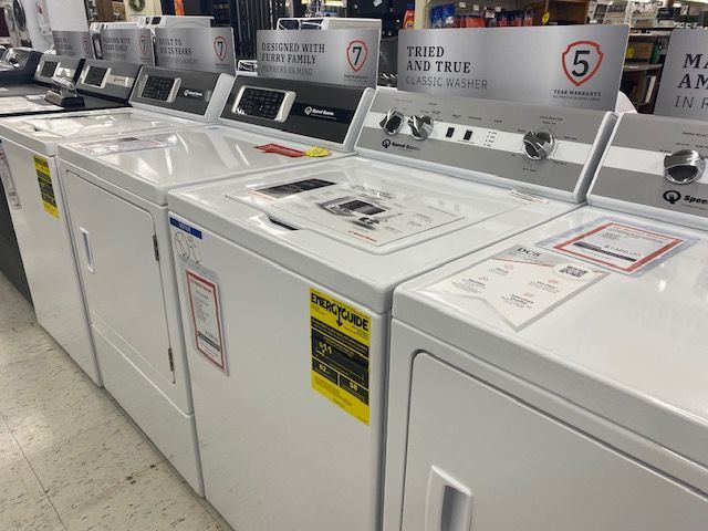 A row of white washers and dryers are lined up in a store.