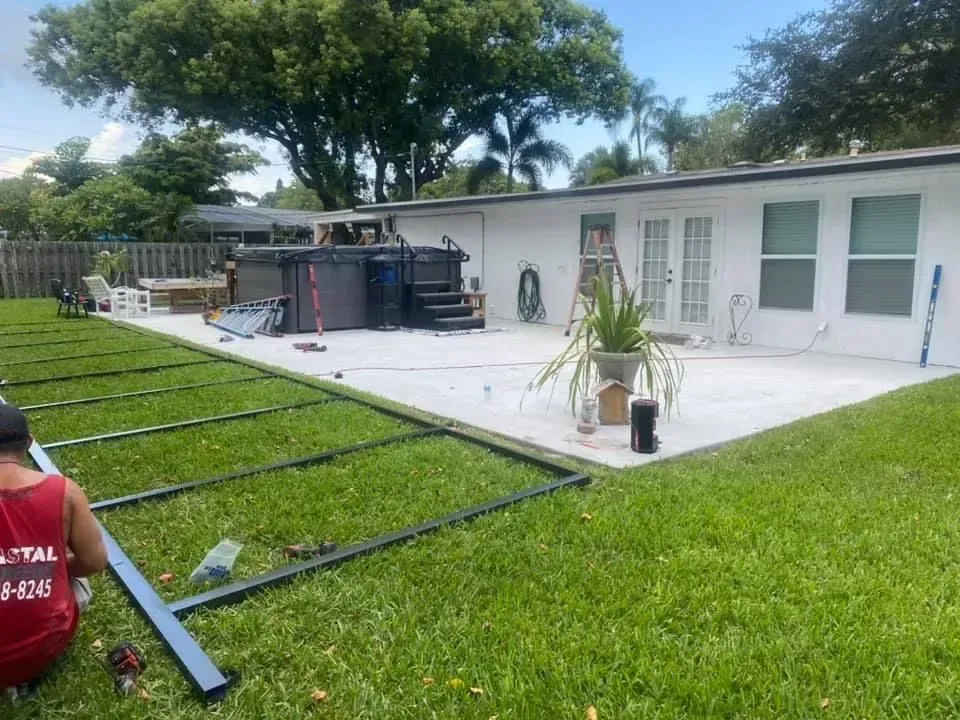 Person assembling fence on grassy yard, with patio and hot tub in the background.
