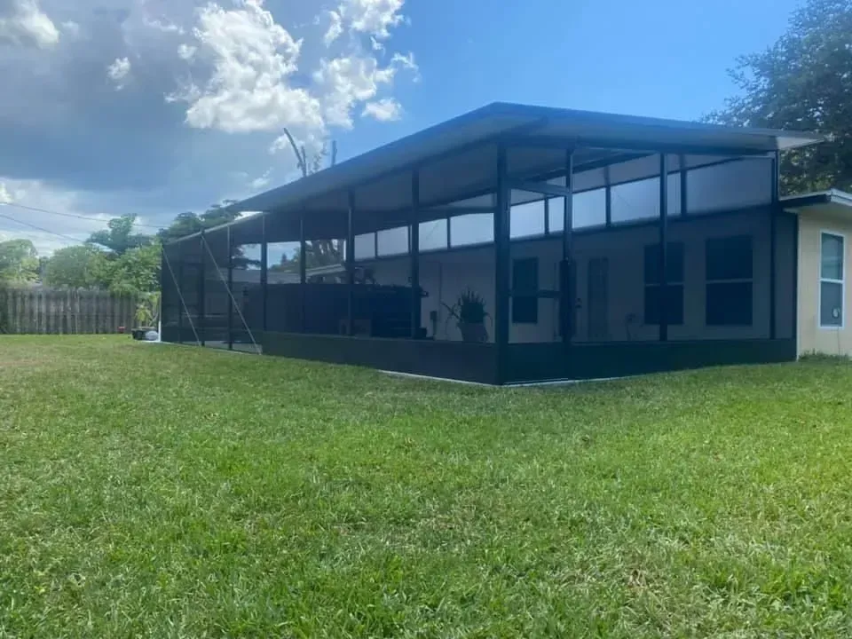 Backyard with a screened-in patio, grass, and a light-colored house under a partly cloudy sky.