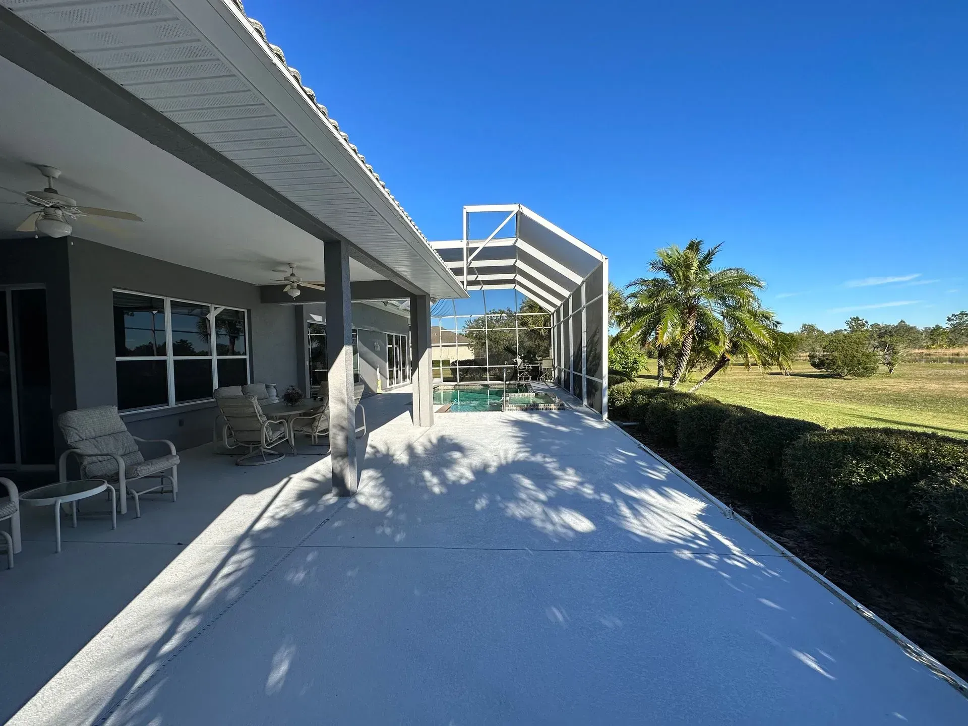 Long gray porch with pool and manicured hedges under a bright blue sky.