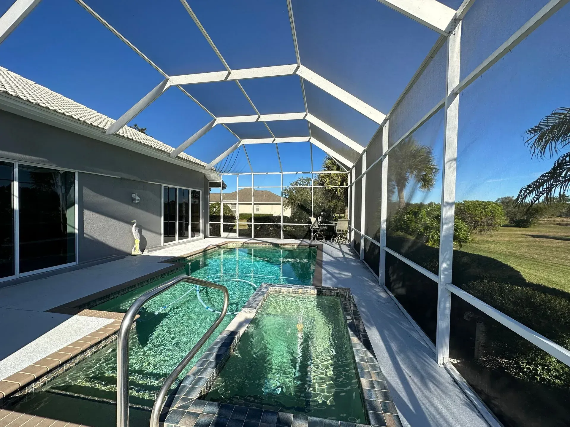 Pool and jacuzzi enclosed by a screen in a sunny backyard.
