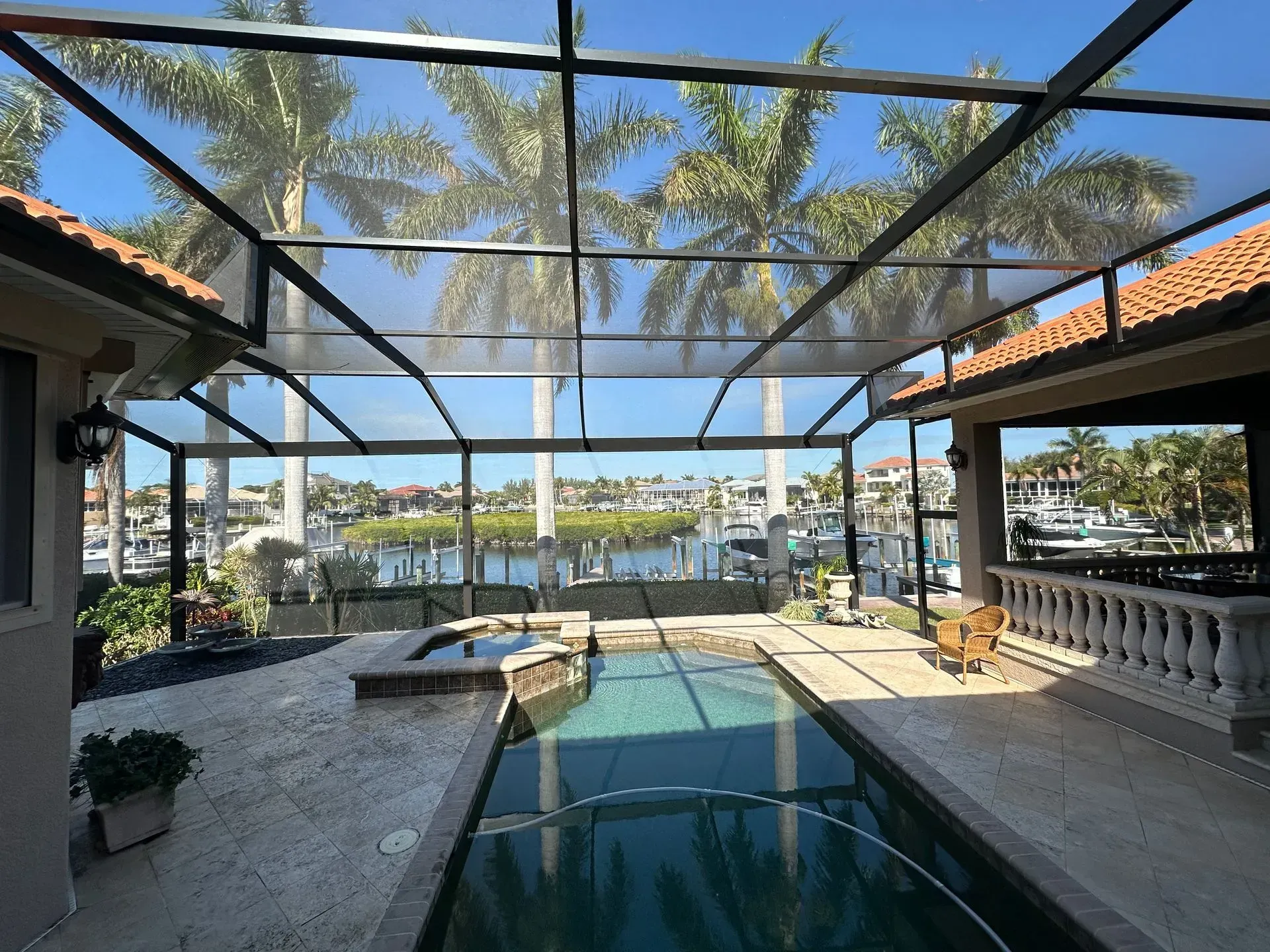 Screened-in pool area with water view, clear sky, palm trees, and boats.