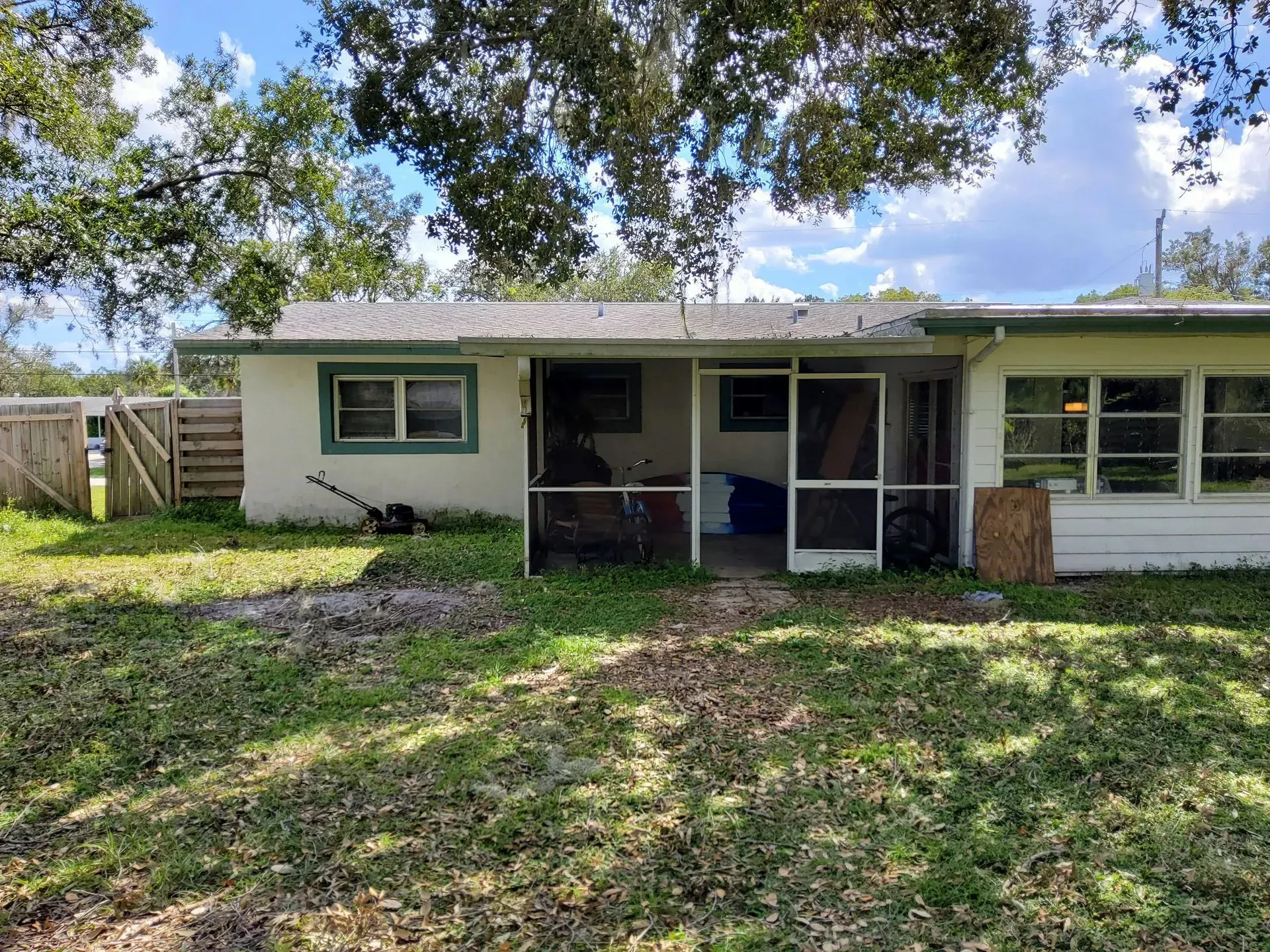 Backyard view of a single-story house with a screened porch and overgrown lawn.
