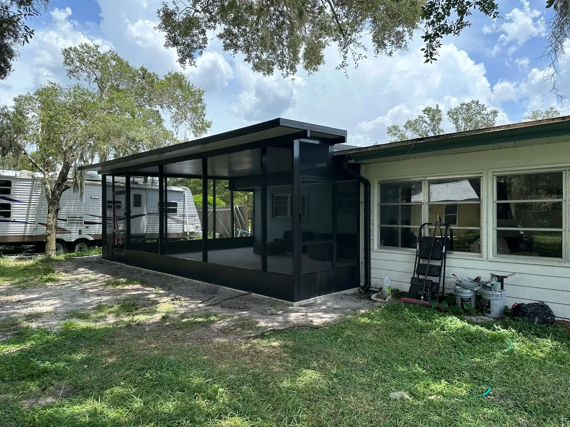Screened-in porch attached to a house, with a parked RV visible on the left.