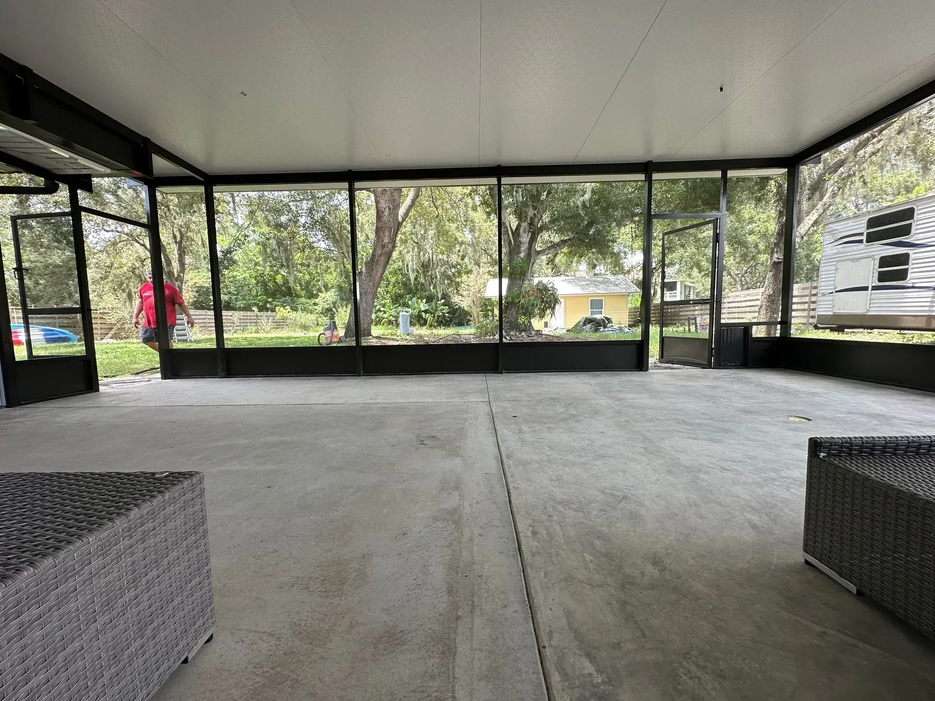 Screened patio with concrete floor, looking out at a yard and RV; two wicker chairs in foreground.