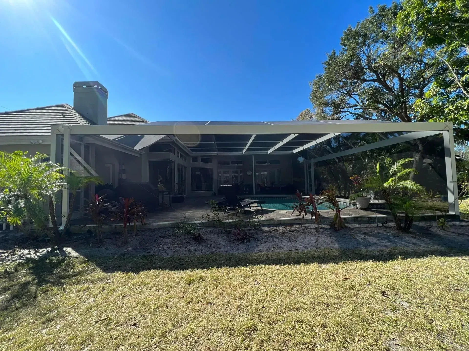Backyard patio with a screen enclosure, pool, and landscaping under a bright blue sky.