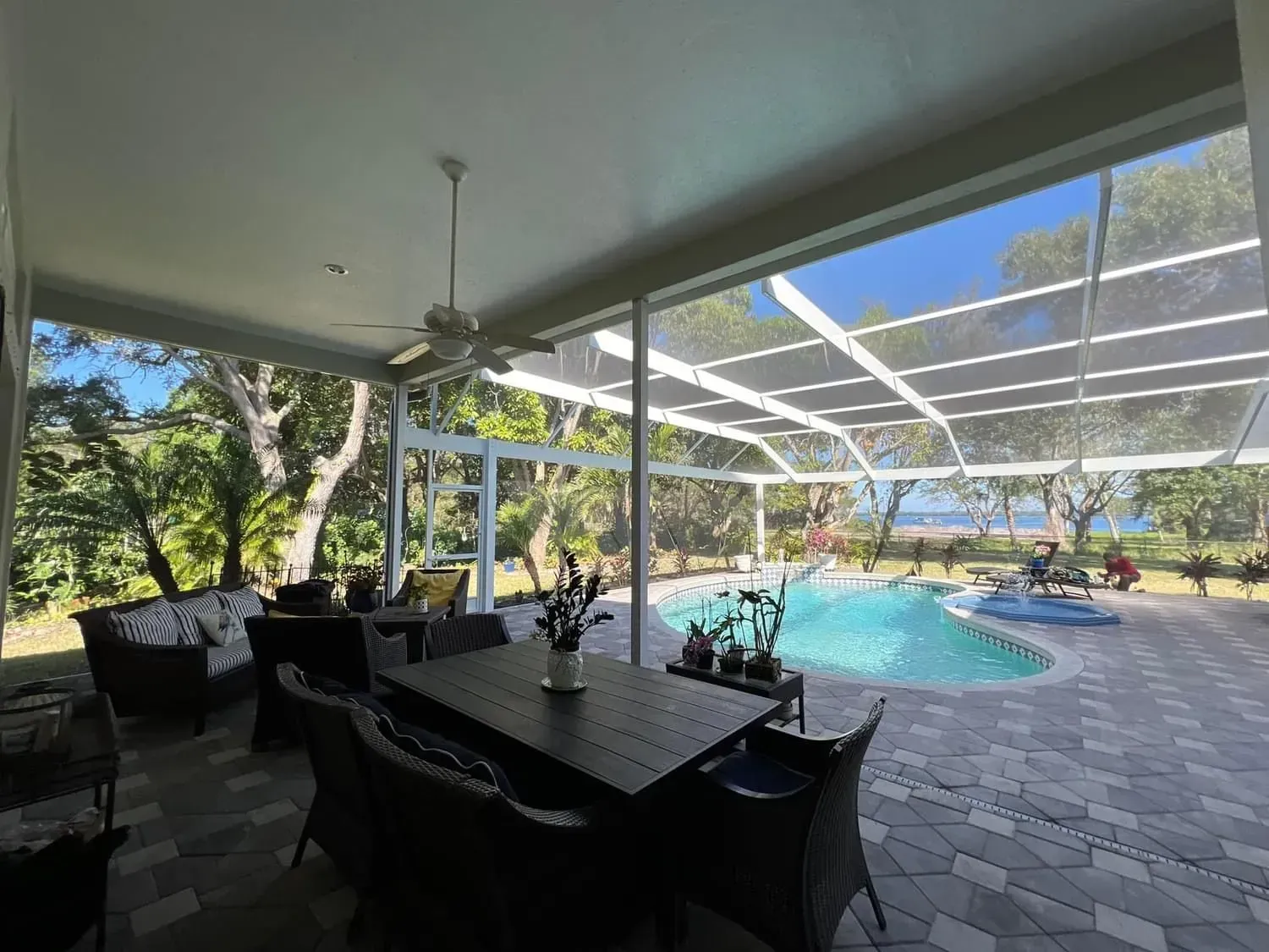 Patio with dark furniture, overlooking a pool and trees, under a white ceiling with a fan.