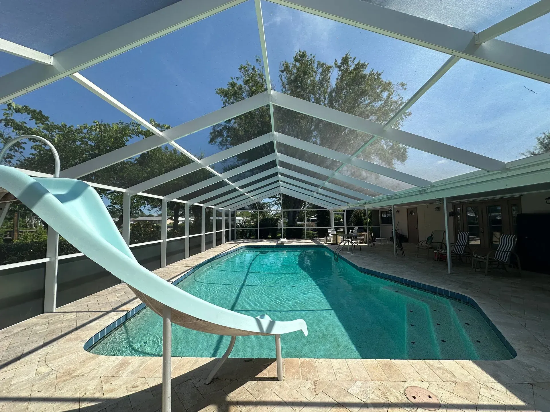 Pool with a water slide under a screened enclosure on a sunny day.