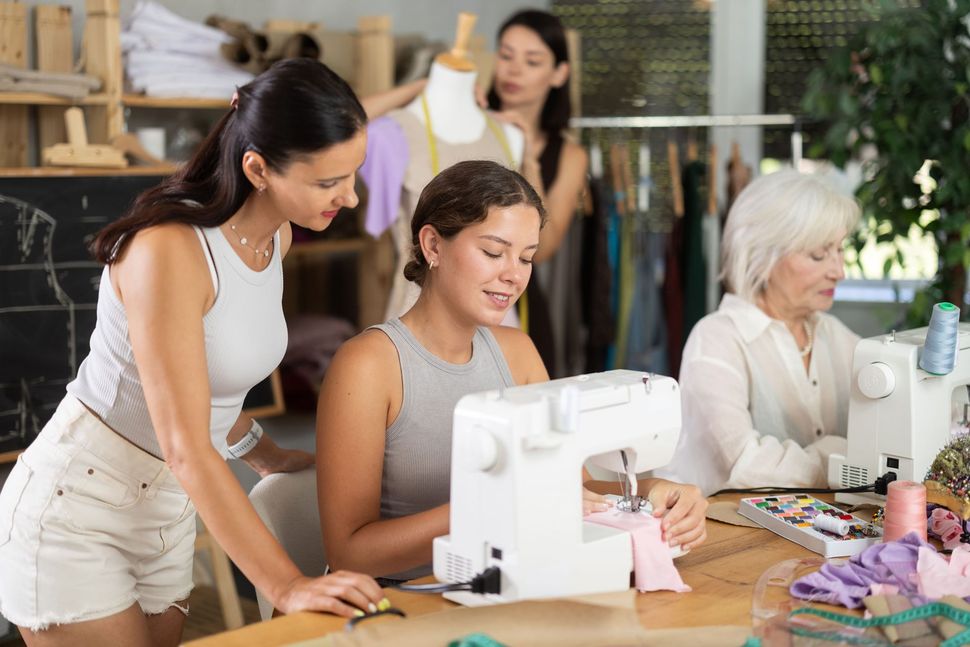 Three people working together at a sewing machine in a bright craft studio