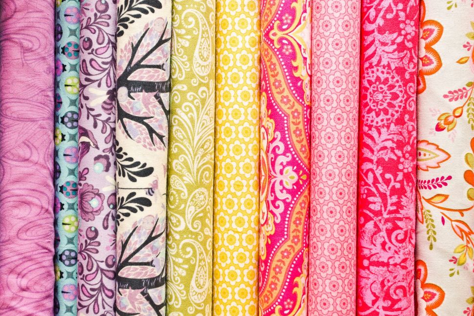 Colorful patterned fabric bolts in pink, yellow, orange, and white arranged upright