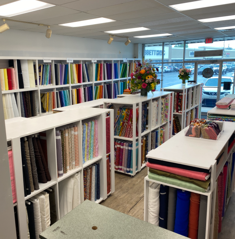 Fabric store interior with rows of colorful bolts of fabric and shelves near a front window