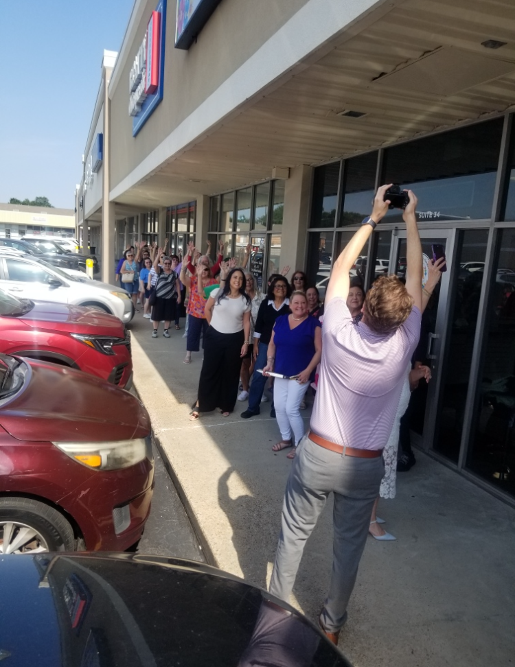 People lined up outside a storefront, with a woman in front holding a phone overhead to take a photo.