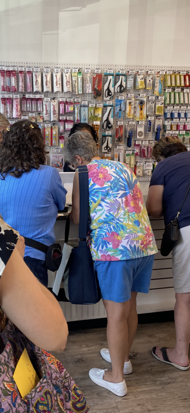Three people browsing a wall of hanging accessories in a shop, viewed from behind.