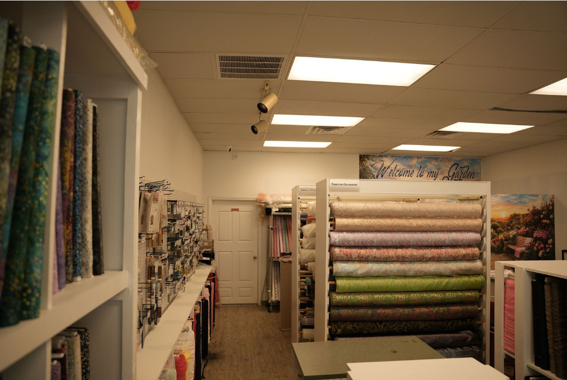 Fabric store aisle with shelves of rolled patterned textiles and bright overhead lights