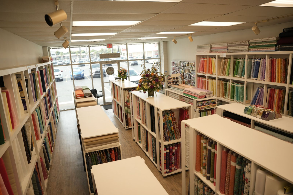 Interior of a bright library aisle with bookshelves and tables, seen toward the front windows.