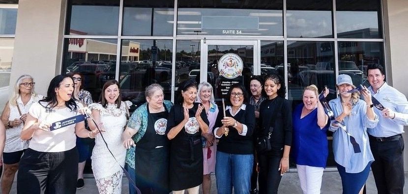 Group of people standing outside a building entrance, smiling and raising drinks in a celebratory toast.