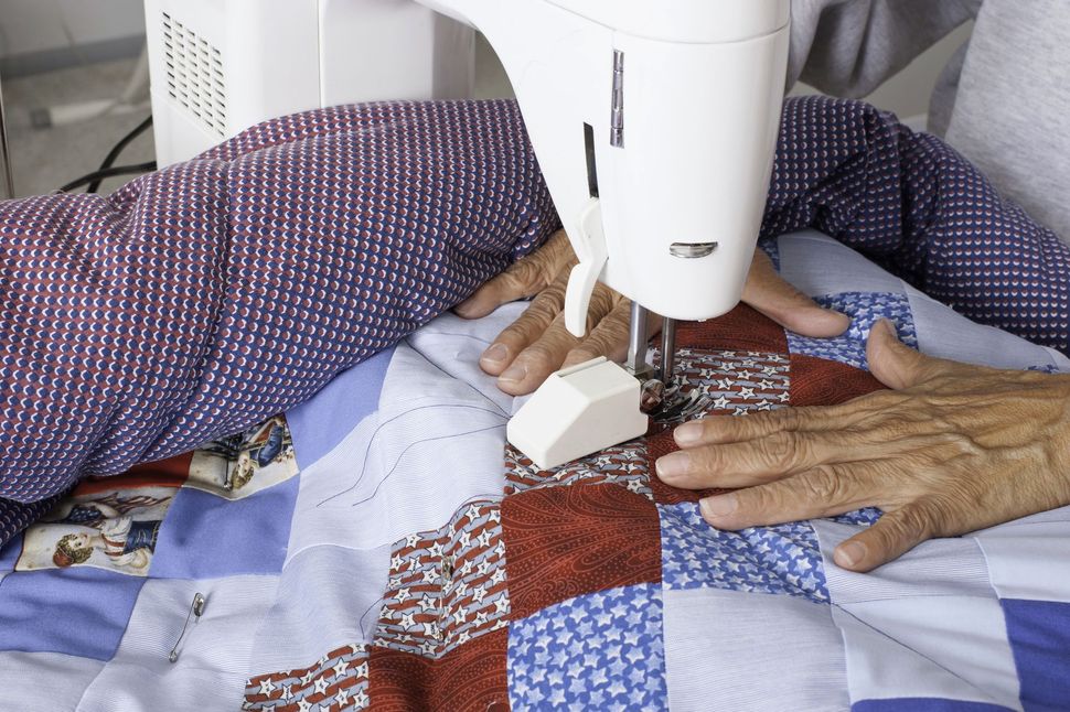 Hands guiding a sewing machine stitching a colorful patchwork quilt