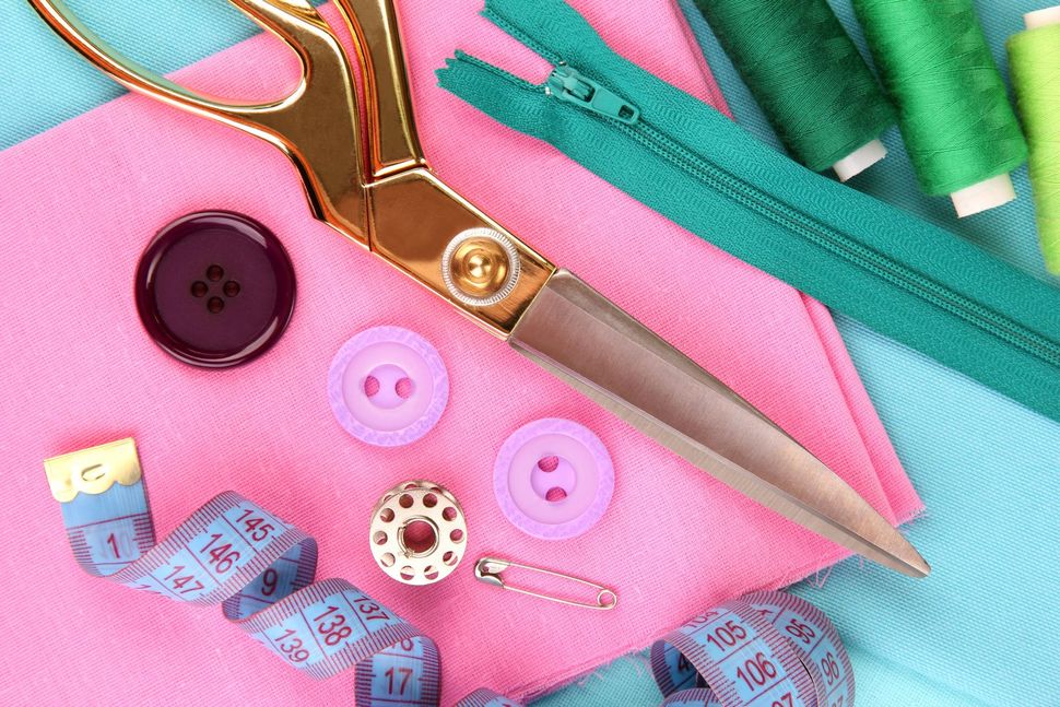 Crafting tools with gold scissors, buttons, thread, and a teal zipper on pink and turquoise fabric
